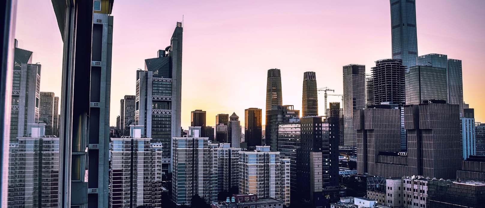High-rise buildings and skyscrapers under a pink and purple sunset sky in an urban cityscape, viewed from an elevated vantage point.
